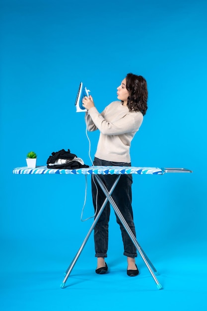 Top view of focused young girl standing behind the board and holding iron on blue wave background