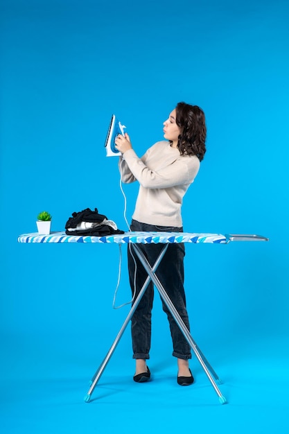 Photo top view of focused young girl standing behind the board and holding iron on blue wave background