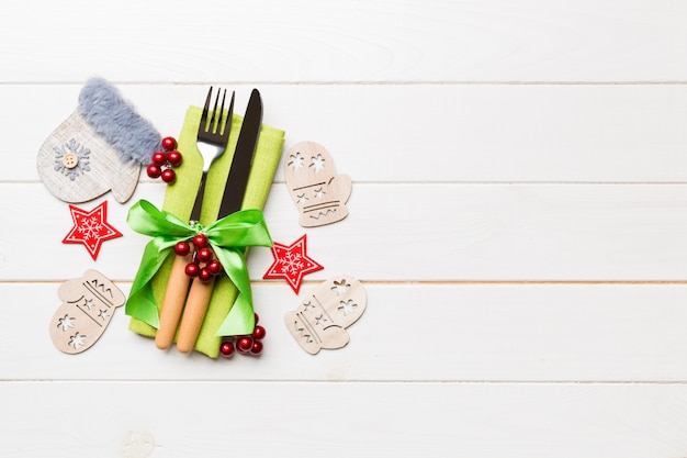 Top view of fork and knife on napkin on wooden background. Different christmas decorations and toys. New Year dinner concept with empty space