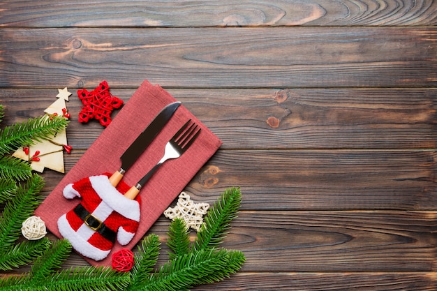 Top view of fork and knife put in santa clothes on napkin with christmas decorations and new year tree