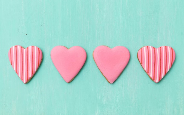 Top view on four pink sugar cookies in heart shape on turquoise wooden background Valentine's day