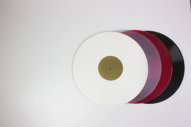 Top view of four vinyls, black, red, blue and white, on white.