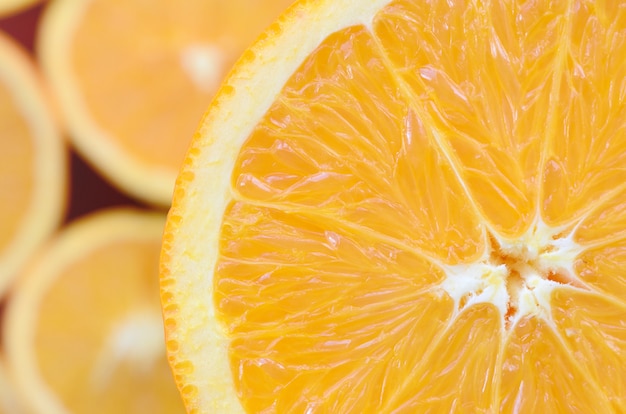 Top view of a fragment of the orange fruit slice on the background of many blurred orange slices. 