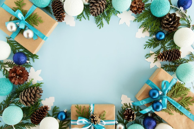 Top view on frame from Christmas decorations gift boxes fir branches pine cones and Christmas lights on the blue background with copy space