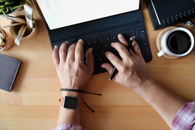 La mano del freelance di vista superiore facendo uso sulla compressa della tastiera sullo spazio di lavoro dello scrittorio.