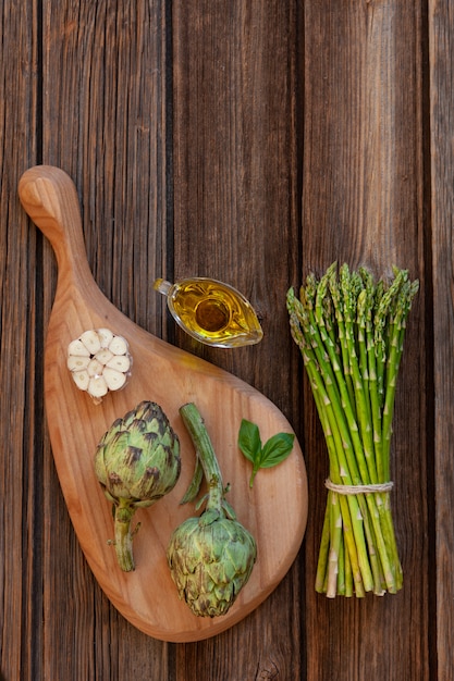 Top view of fresh artichoke and Bunch of green asparagus with garlic and olive oil on wooden table