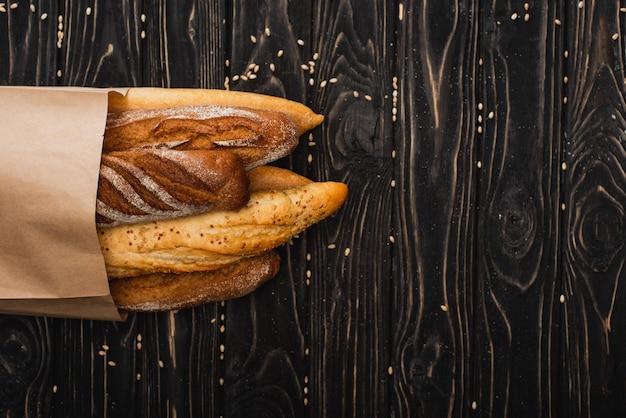 Top view of fresh baked baguette loaves in paper bag on wooden black surface