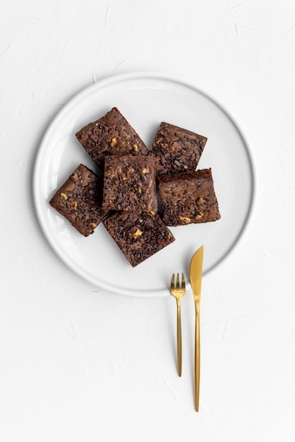 Top view of fresh brownie pieces on white plate with golden cutlery