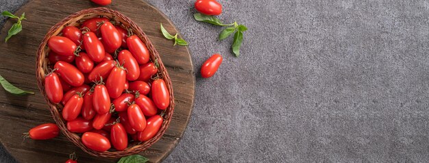 Top view of fresh cherry tomatoes in a basket with basil leaf on gray table background.