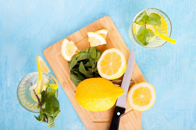 Top view of fresh cut lemons next to two glasses with lemonade on a blue vintage wooden board