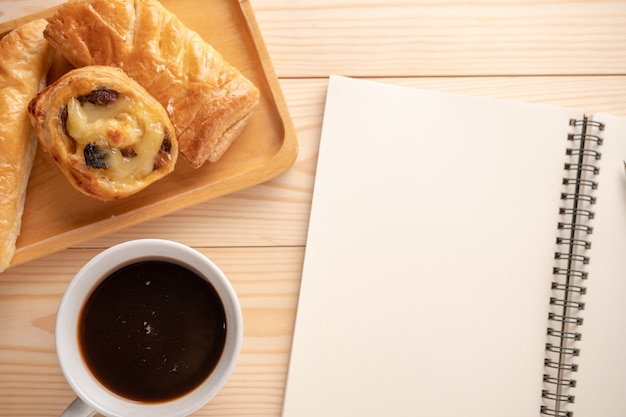 Top view of fresh desserts and pies placed on wooden trays Placed beside a blank notebook And white coffee mugs. 