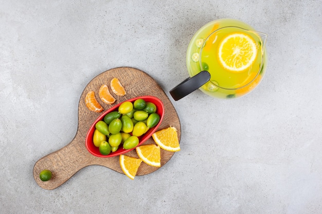 Top view of fresh fruit lemonade with a pile of kumquats with orange and tangerine slices on wooden board.