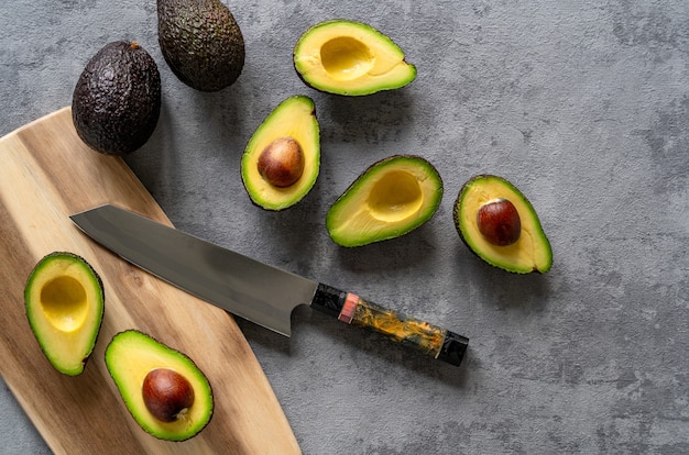 Top view of fresh halved and whole avocados on a grey surface, with a cutting board and knife