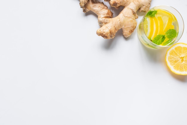 Top view of fresh lemonade in glass near lemon and ginger root on white background