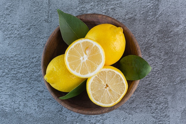 Top view of fresh lemons in wooden bowl over grey.