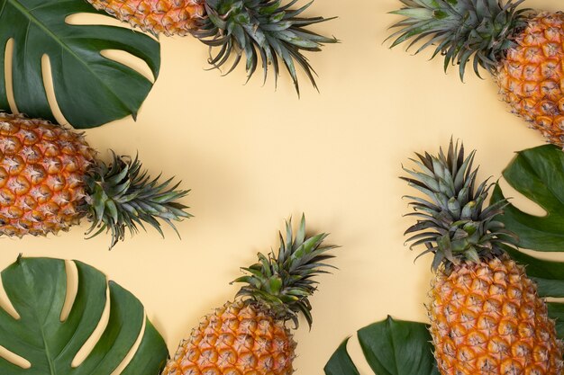 Вид сверху свежего ананаса с тропической пальмой и листьями монстеры на желтом фоне стола.