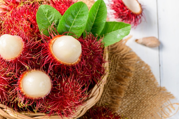 Photo top view of fresh rambutan fruits with leaves on bamboo basket on wood background