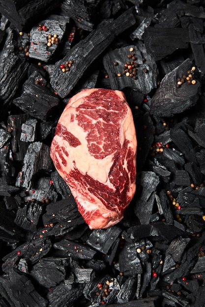 Top view of fresh raw steak on black coals with peppercorns