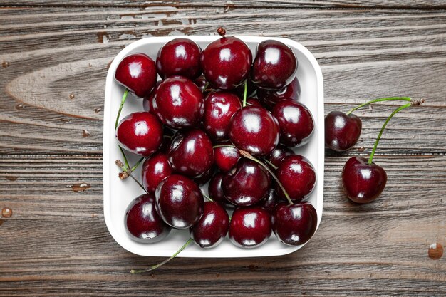 Top view of fresh ripe juicy sweet cherries in a white plate on wooden background Wet sweet cherries