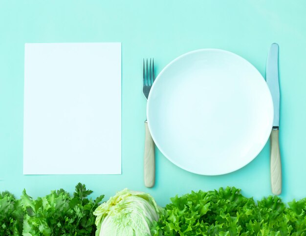 Top view fresh salad cabbage herbs empty plate fork knife white paper card on green background