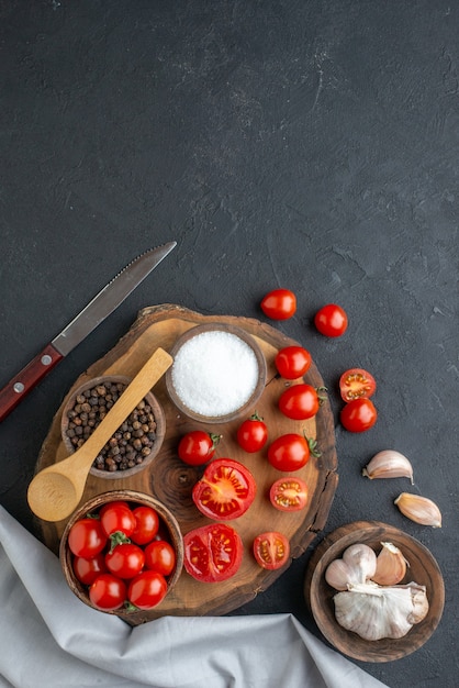 Top view of fresh tomatoes and spices on wooden board white towel garlics on black surface