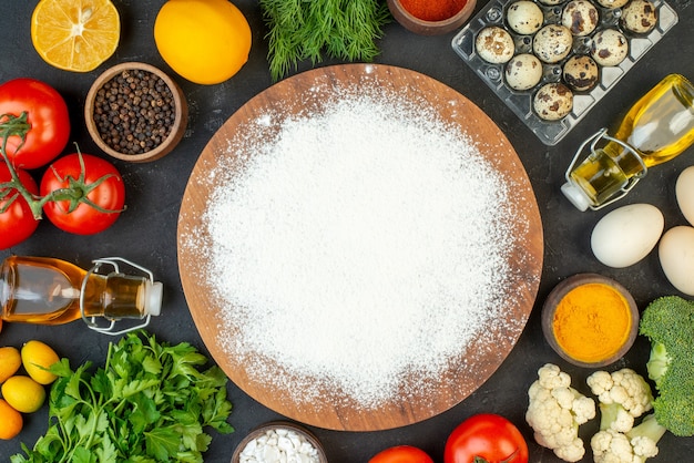 Top view of fresh vegetables fallen oil bottle pepper a green bundle eggs flour on wooden cutting board on black background