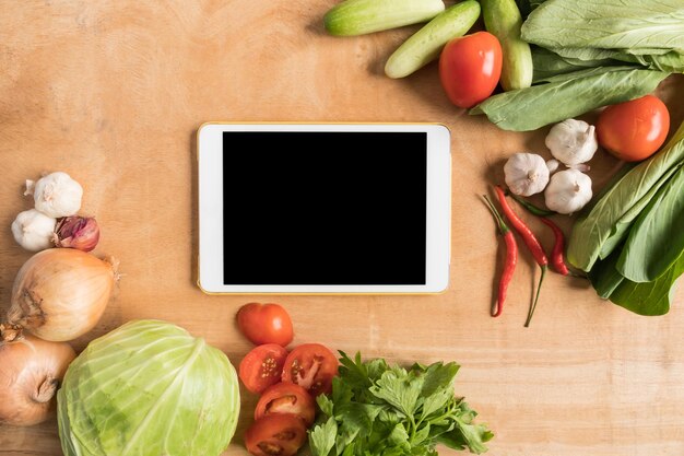 top view of fresh vegetables with tablet touch computer gadget on wooden table background