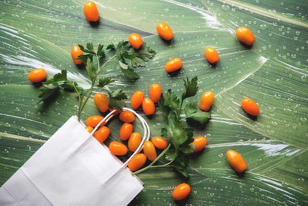 Top view on fresh yellow orange cherry tomatoes in white paper bag on green leaves background