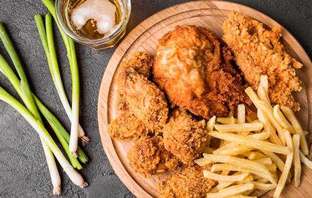 Photo top view fried chicken with fries on cutting board and green onions