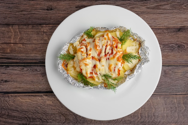 Top view of fried in foil sea fish and potato with paprica and cheese on wooden table