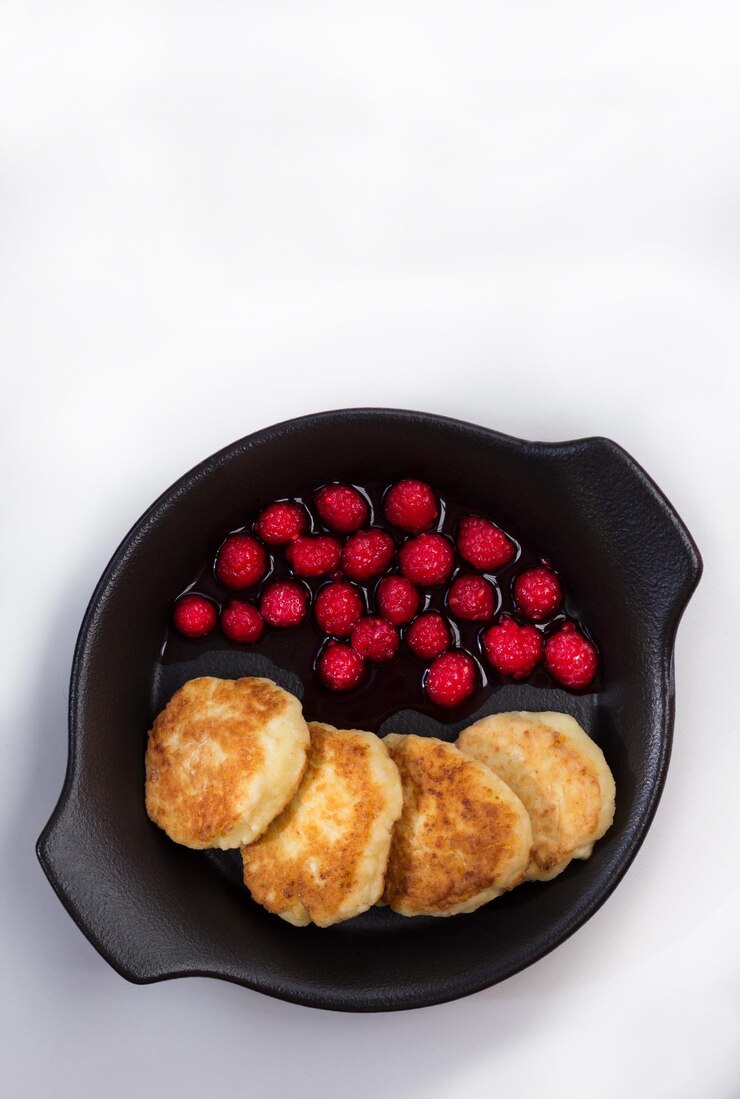 Photo top view of fried homemade syrniki with fresh raspberry on black plate on the white background