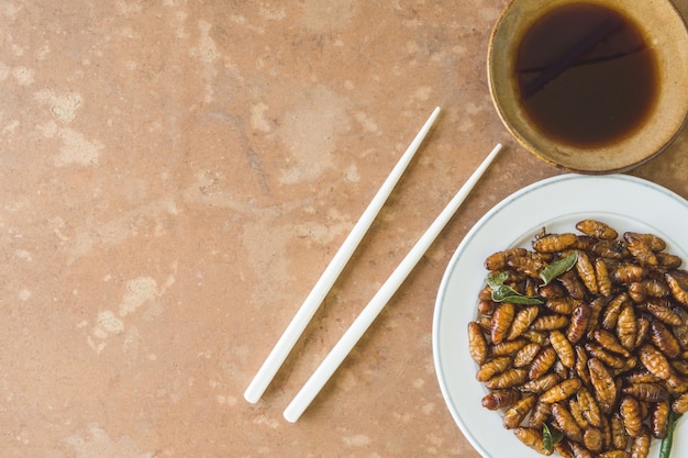 Top view of Fried insects in dish with sauce on wooden table. copy space