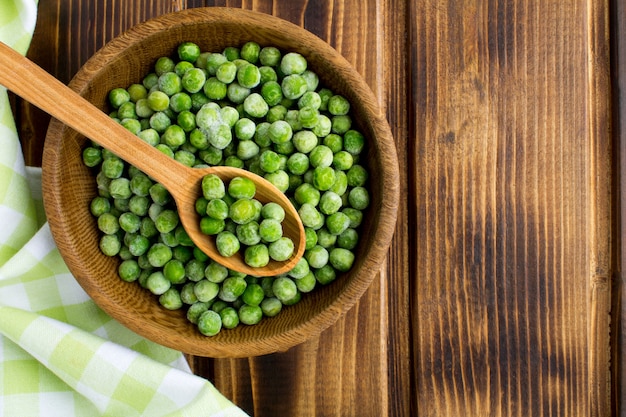 Top view of frozen peas in the brown bowl on the wood table