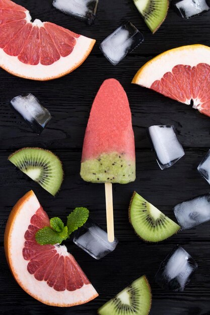 Top view of fruit popsicle stick with kiwi and grapefruit on the black wooden  background Copy space