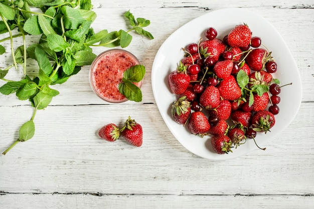 Top view of fruit smoothie with strawberries and cherries and mint on white wooden background