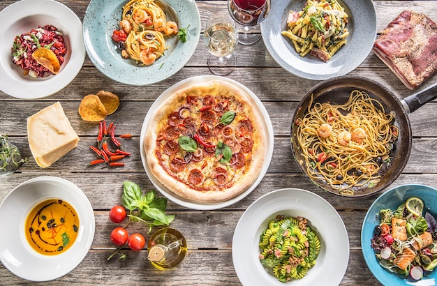 Foto tavolo completo di vista dall'alto di piatti italiani su piatti e padella. pizza pasta risotto zuppa e insalata di verdure di pesce.