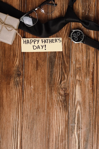 Вид сверху на подарочную коробку, поздравительную открытку с надписью "счастливый день отца" и мужские наручные часы с черным галстуком