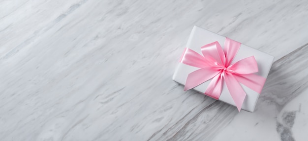 Top view of gift box with pink ribbon on white marble.