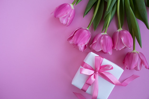 Top view of gift and pink tulips on the pink surface