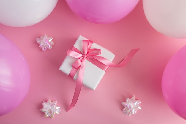 Top view of gift with pink and white balloons on the pink