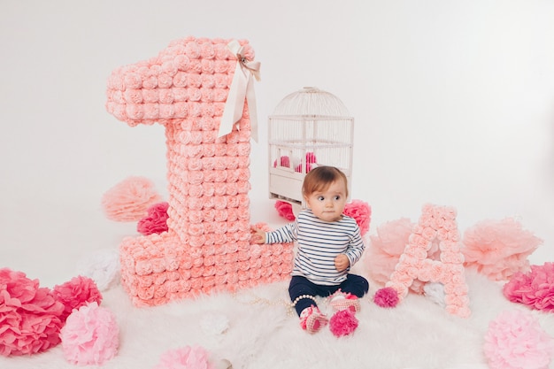 Top view: the girl child mother sitting on the floor among the numbers 1, artificial flowers and a bird cage