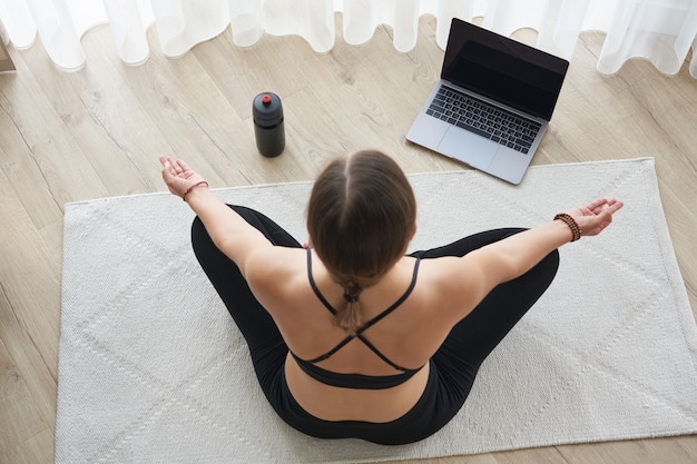 Top view of girl relaxing in lotus pose at home with laptop yoga concept