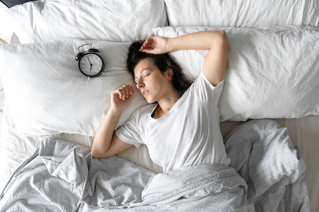 Top view of a girl sleeping next to an alarm clock. Time to wake up. On the wake-up clock 7 a.m. Deep sleep.