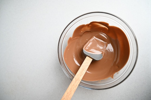 Top view of glass bowl spatula and tempering molten\
chocolatethe process of tempering chocolate and making\
chocolates