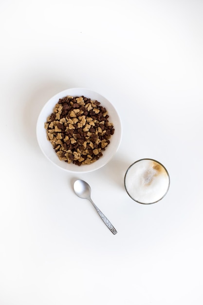 Top view of glass of coffee latte and cornflakes in bowl with spoon isolated on white