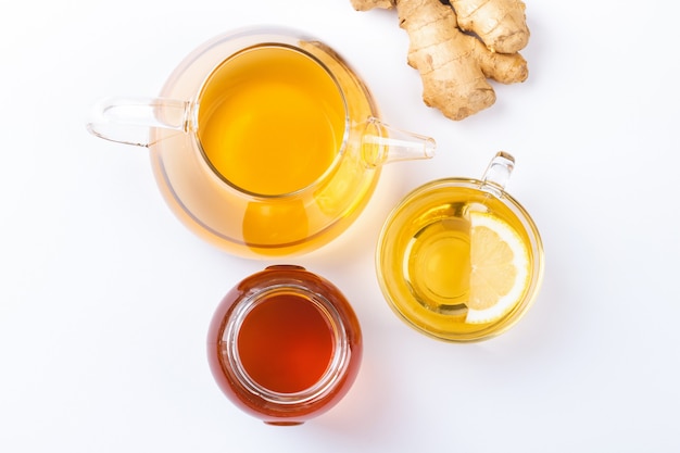 Top view of glass cup with ginger and lemon tea, teapot, honey, white background. Homemade natural remedy against flu, cold, cough. Immunity stimulating hot beverage, natural medicine for good health