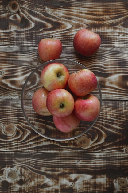 Вид сверху на стеклянную тарелку с яблоками, стоящую на деревянном столе, на который упали два яблока