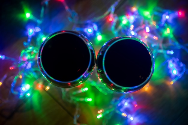 Top view of glass wine glasses in shining christmas garland on dark background