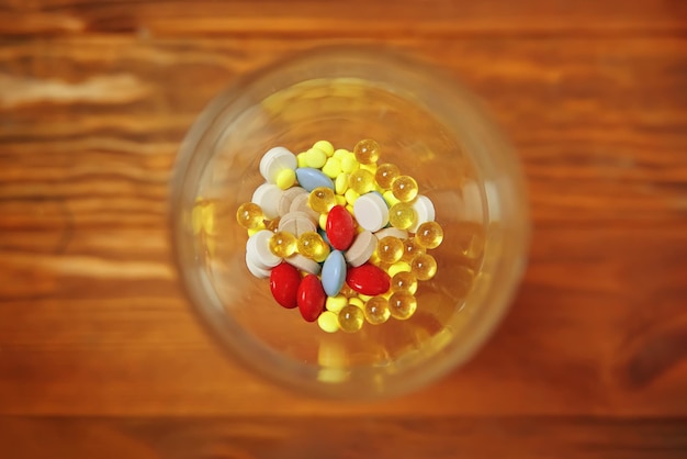 Top view of glass with drugs and pills inside vitamins in goblet on orange wooden table copy space f...