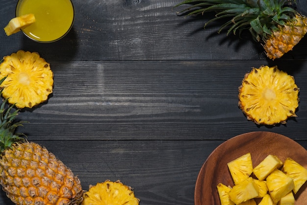 Top view of glasses of pineapple juice and pineapple fruit on a black wooden table